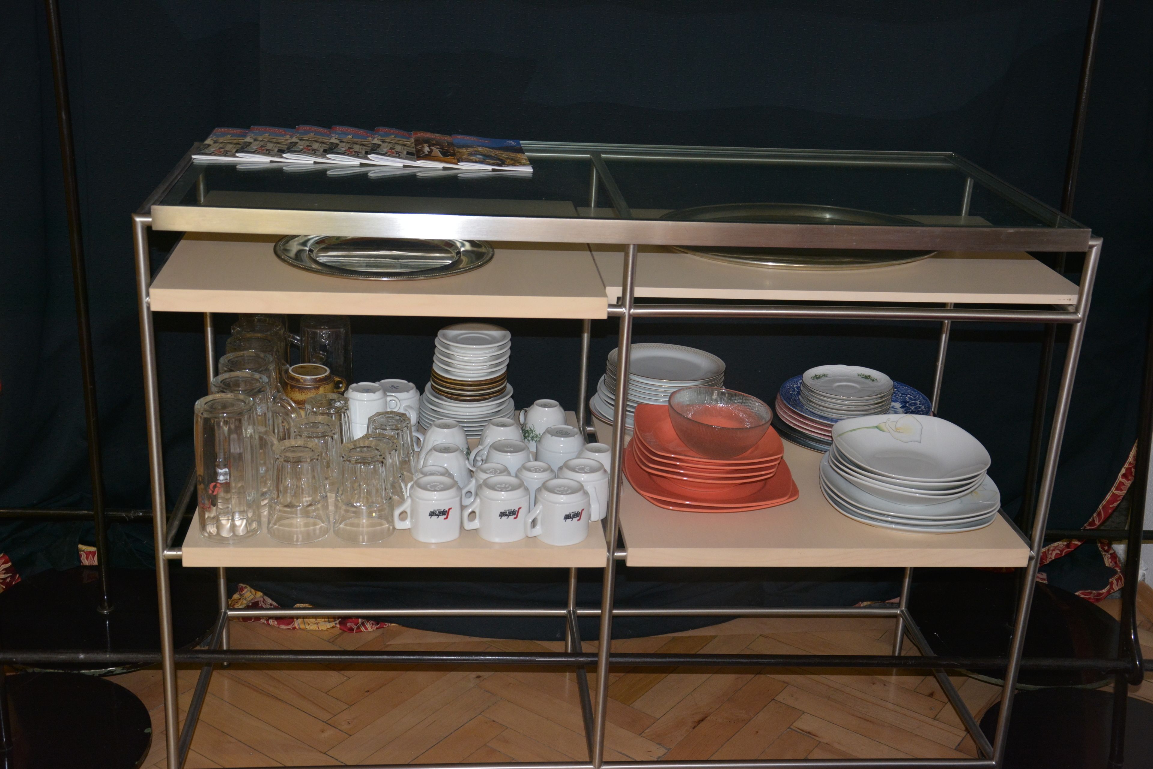Un carro de buffet metálico con varias estanterías, cada una con pilas de platos, tazones y cristalería.