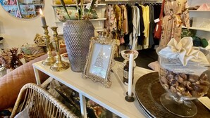 A well-organized retail space with shelves of clothing, a display table with decorative items, and a wicker chair.
