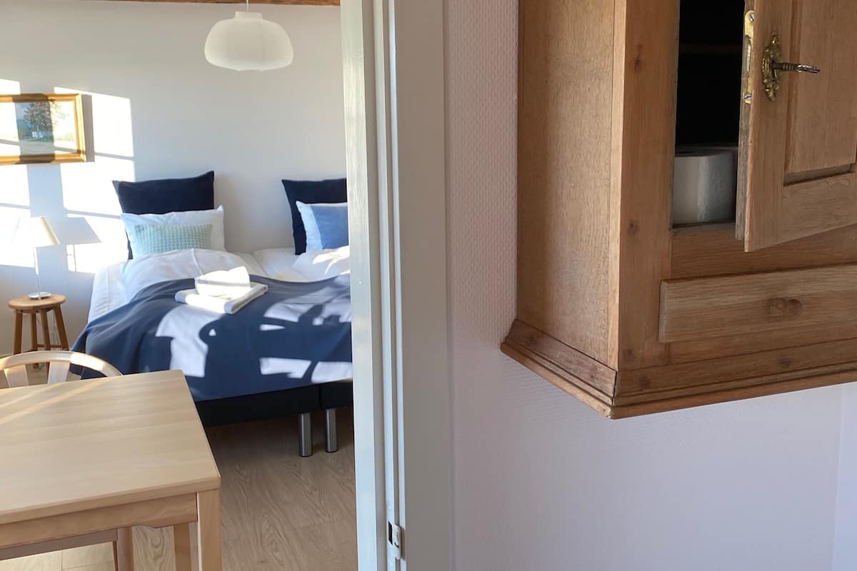 A bedroom with a bed, bedside table, chair, and a wooden cabinet.