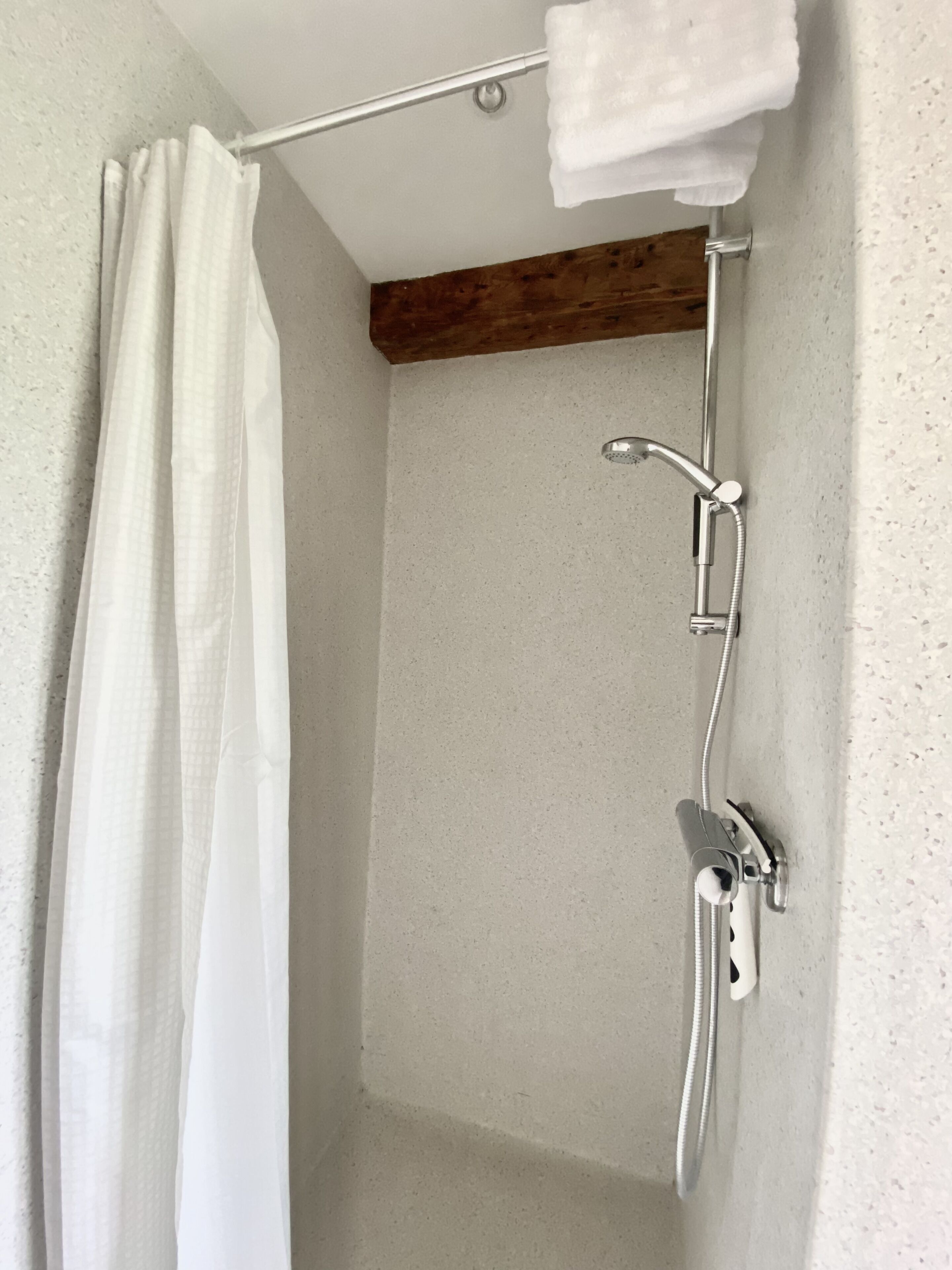 Ducha con cortina, toallero y viga de madera.