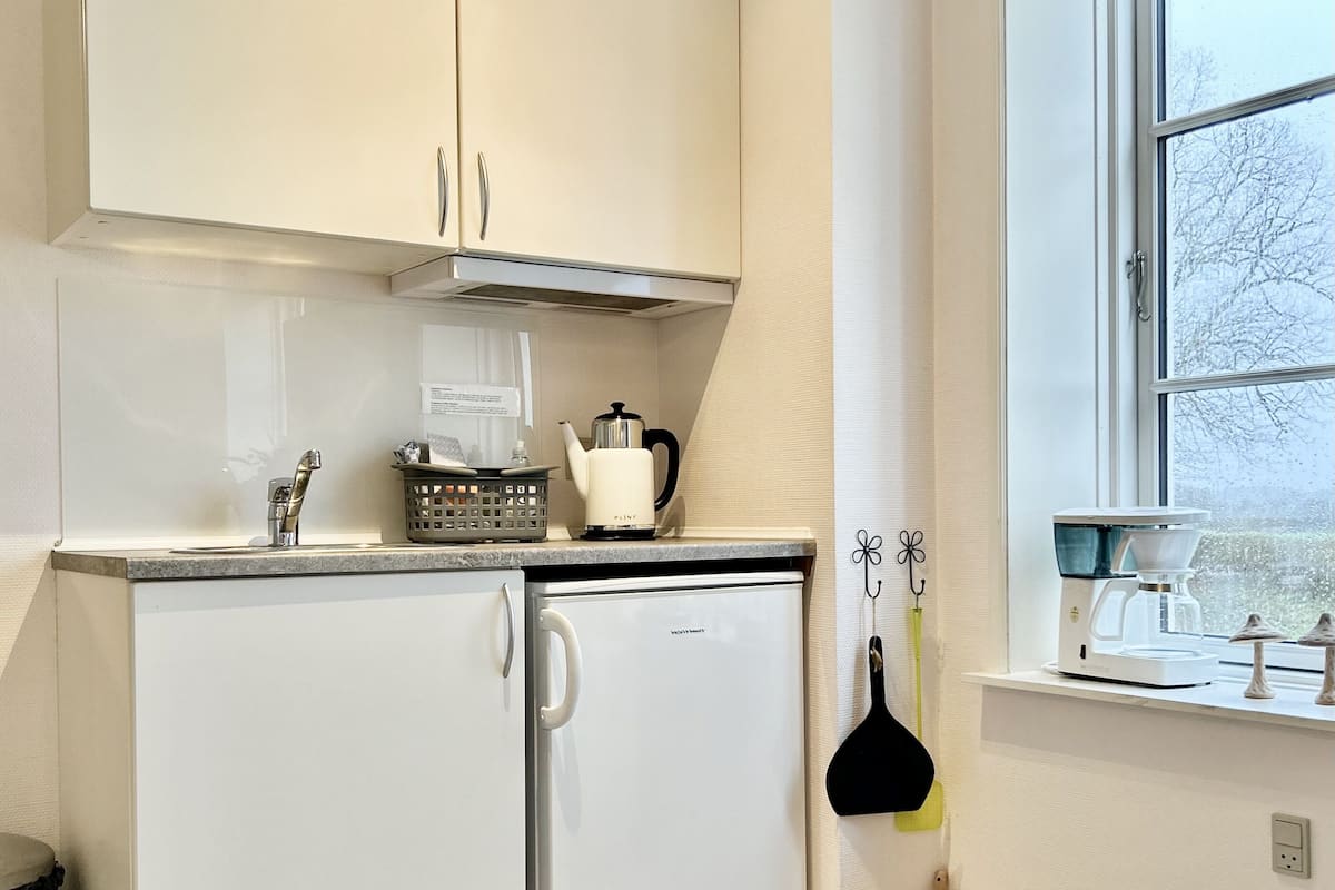 A compact kitchen with white cabinetry, a built-in oven, and a coffee maker on the countertop.