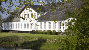 A white building with multiple windows and a sloped roof, situated next to a body of water.