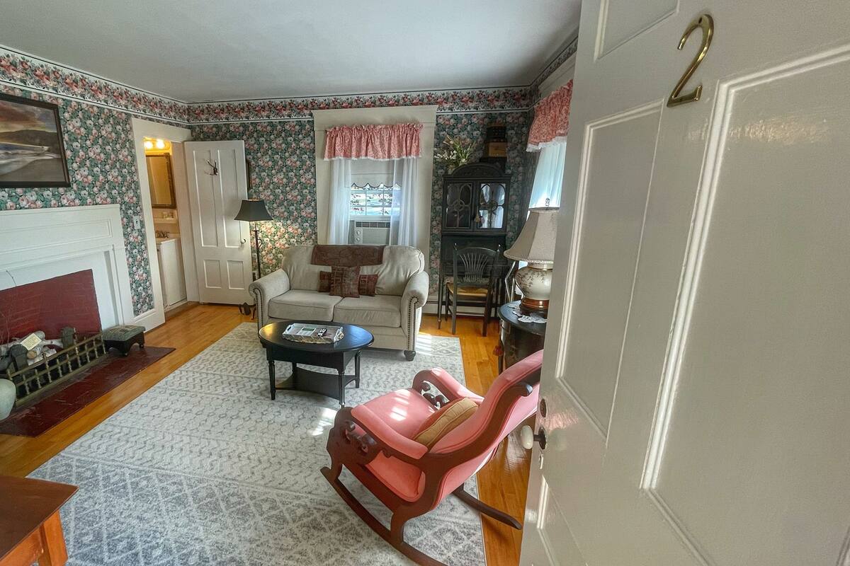 A cozy living room with a fireplace, a sofa, a rocking chair, and a dining area.