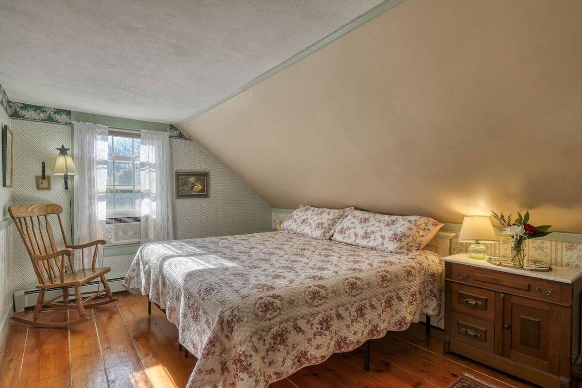 A bedroom with a bed, a rocking chair, a dresser, and a window with curtains.