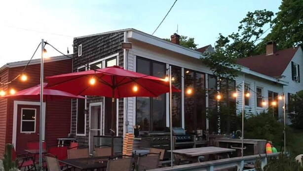A covered outdoor seating area with tables and chairs, a barbecue grill, and string lights. - Open Hearth Inn (Trenton)