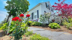 A white house with black shutters, surrounded by lush greenery and a large wooden wheel. - Open Hearth Inn (Trenton)