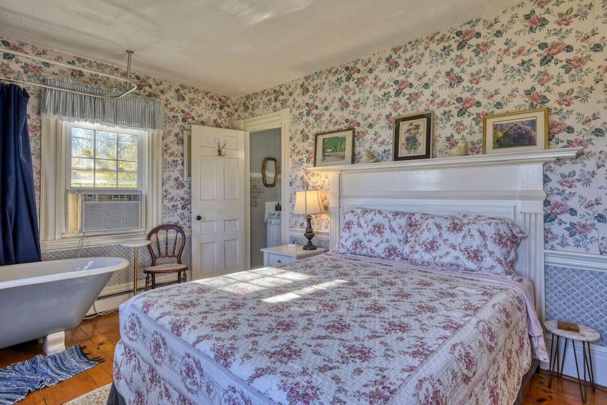 A bedroom with a large bed, a vintage bathtub, and floral wallpaper.