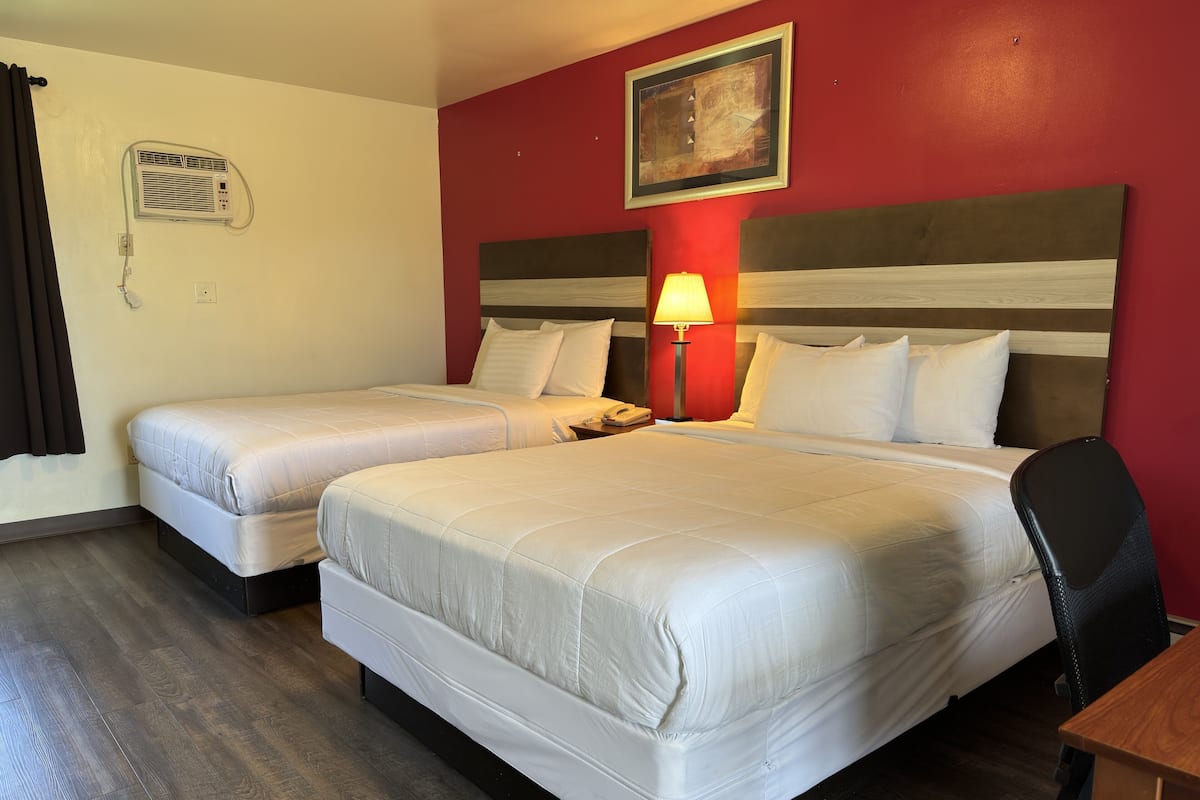 A hotel room with two beds, a nightstand with a lamp, a telephone, and a painting on the wall.