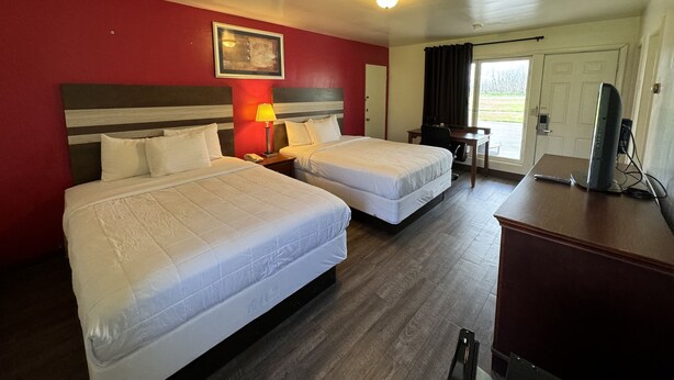 A hotel room with two beds, a desk, a chair, a TV, and a door leading outside. - Holiday Motel Westfield (Westfield)