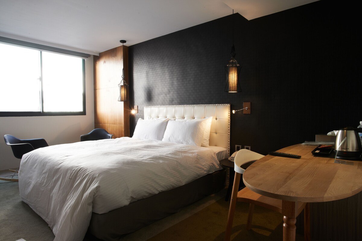 A modern hotel room with a large bed, a desk, and a chair.