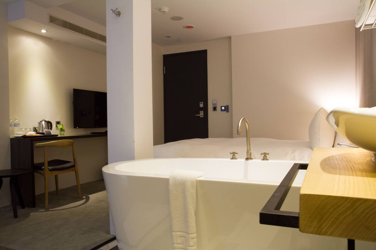 Une salle de bain moderne avec une baignoire sur pieds, un meuble-lavabo en bois, une chaise et un téléviseur à écran plat fixé au mur.