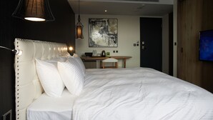 Une chambre d’hôtel avec un grand lit, un bureau, une chaise, une télévision et une œuvre d’art accrochée au mur.