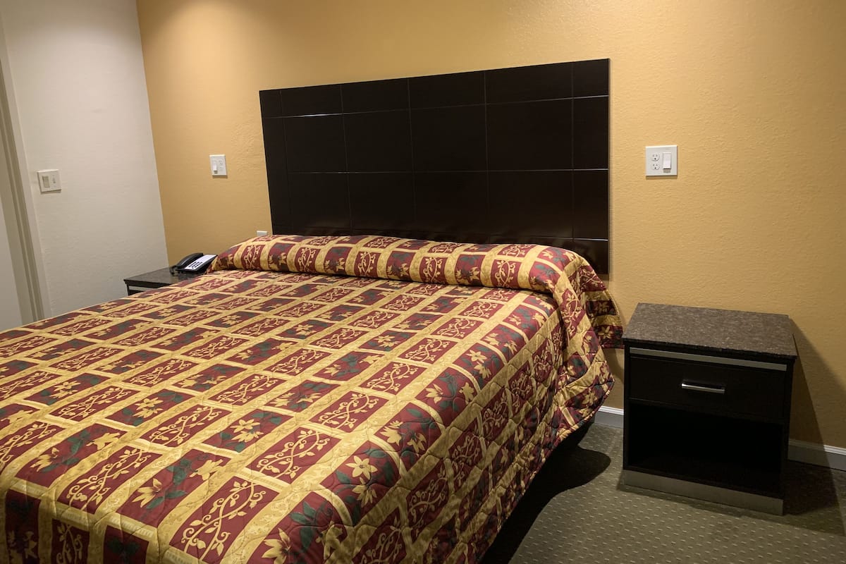 Een hotelkamer met een groot bed, een zwart hoofdbord, een nachtkastje met een telefoon en een klein dressoir.