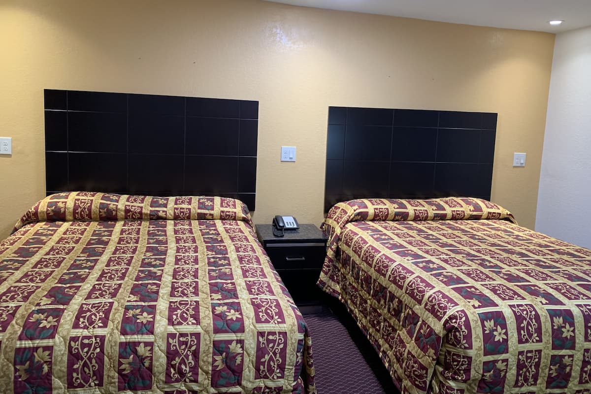 Een hotelkamer met twee bedden, elk met een bedovertrek met dessin en een zwart hoofdbord. Er is een nachtkastje met een telefoon en een stopcontact.