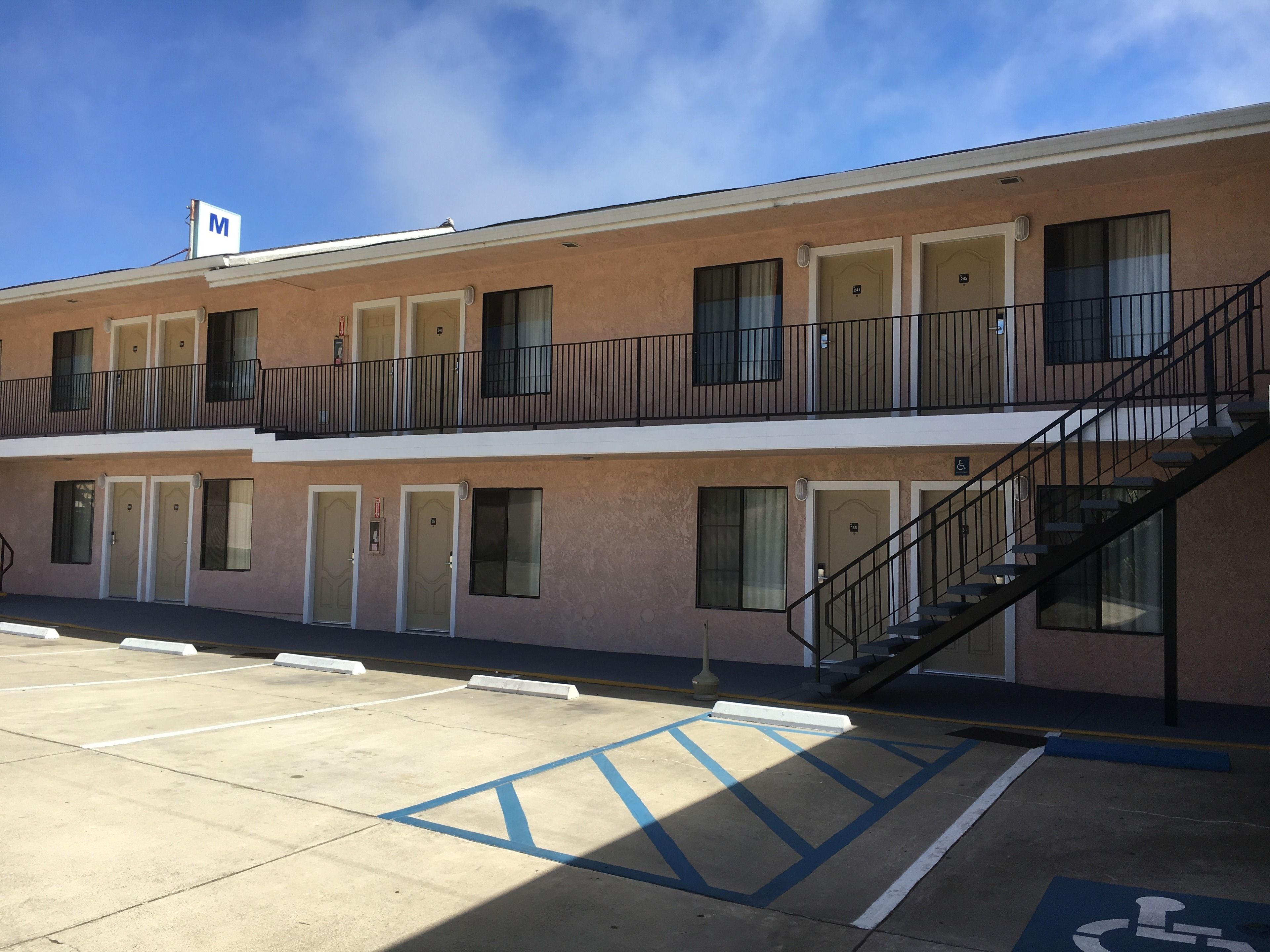 A multi-story motel with a parking lot, marked handicap parking, and a stairway to the upper level.