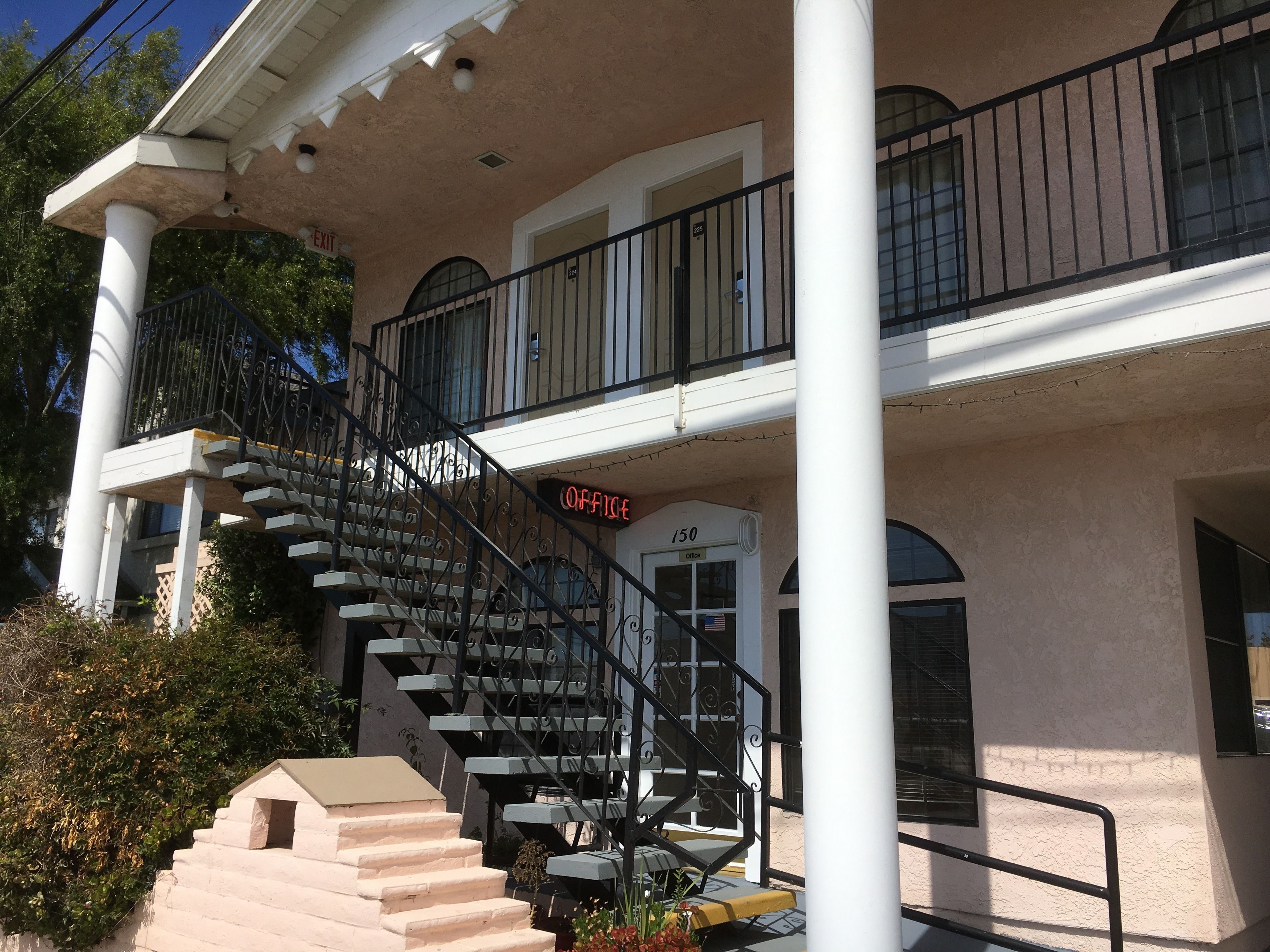 A building with a beige exterior, a staircase leading to a balcony, and a sign indicating an office.