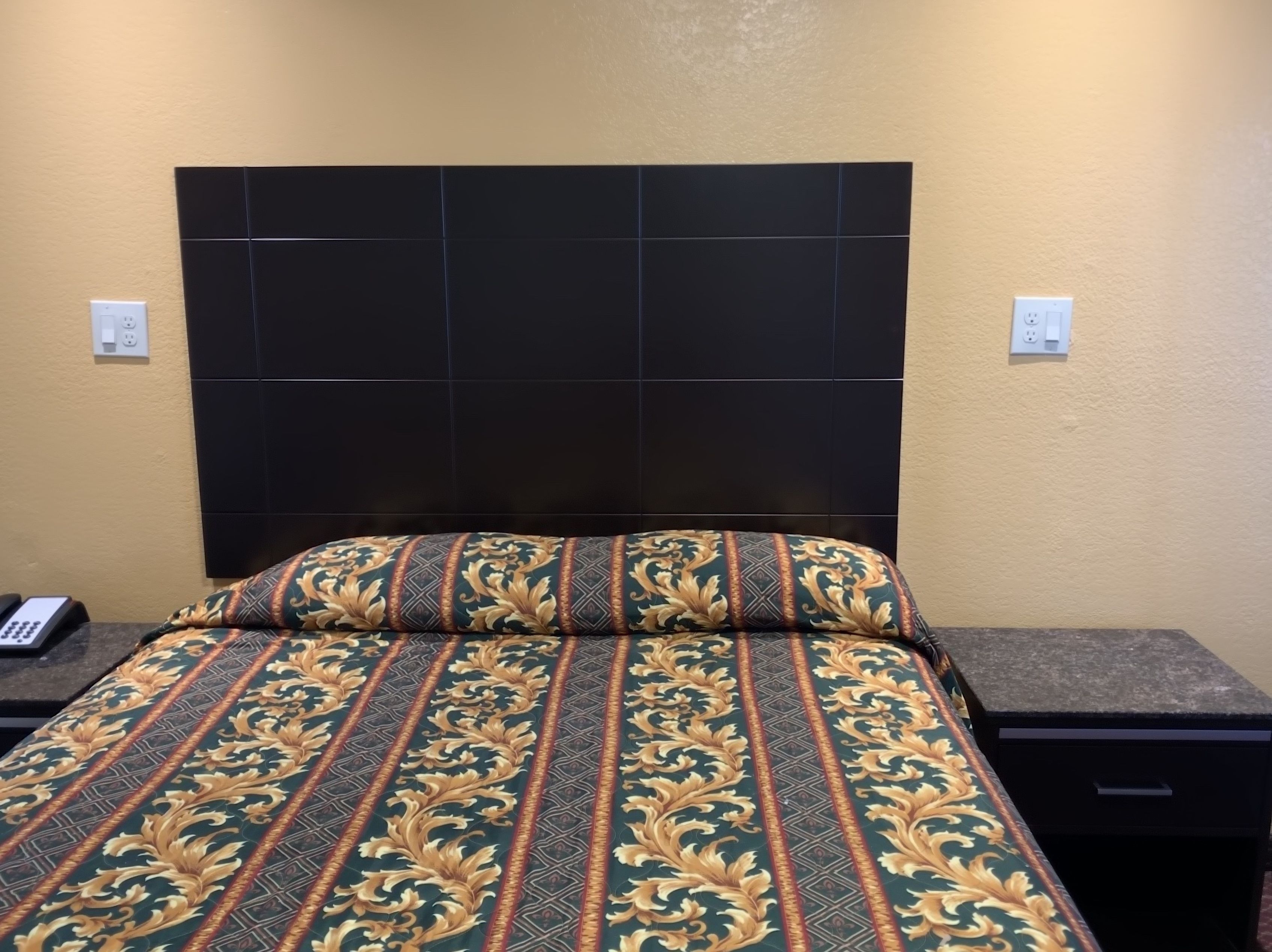 Habitación de hotel con una cama grande, un cabecero oscuro y una mesita de noche con un teléfono.