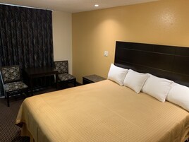 Habitación de hotel con una cama grande, dos sillas, una mesita y un cortinaje estampado.