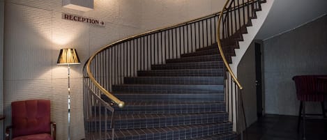 Una escalera curva con barandilla de metal que lleva a una recepción indicada con un cartel.