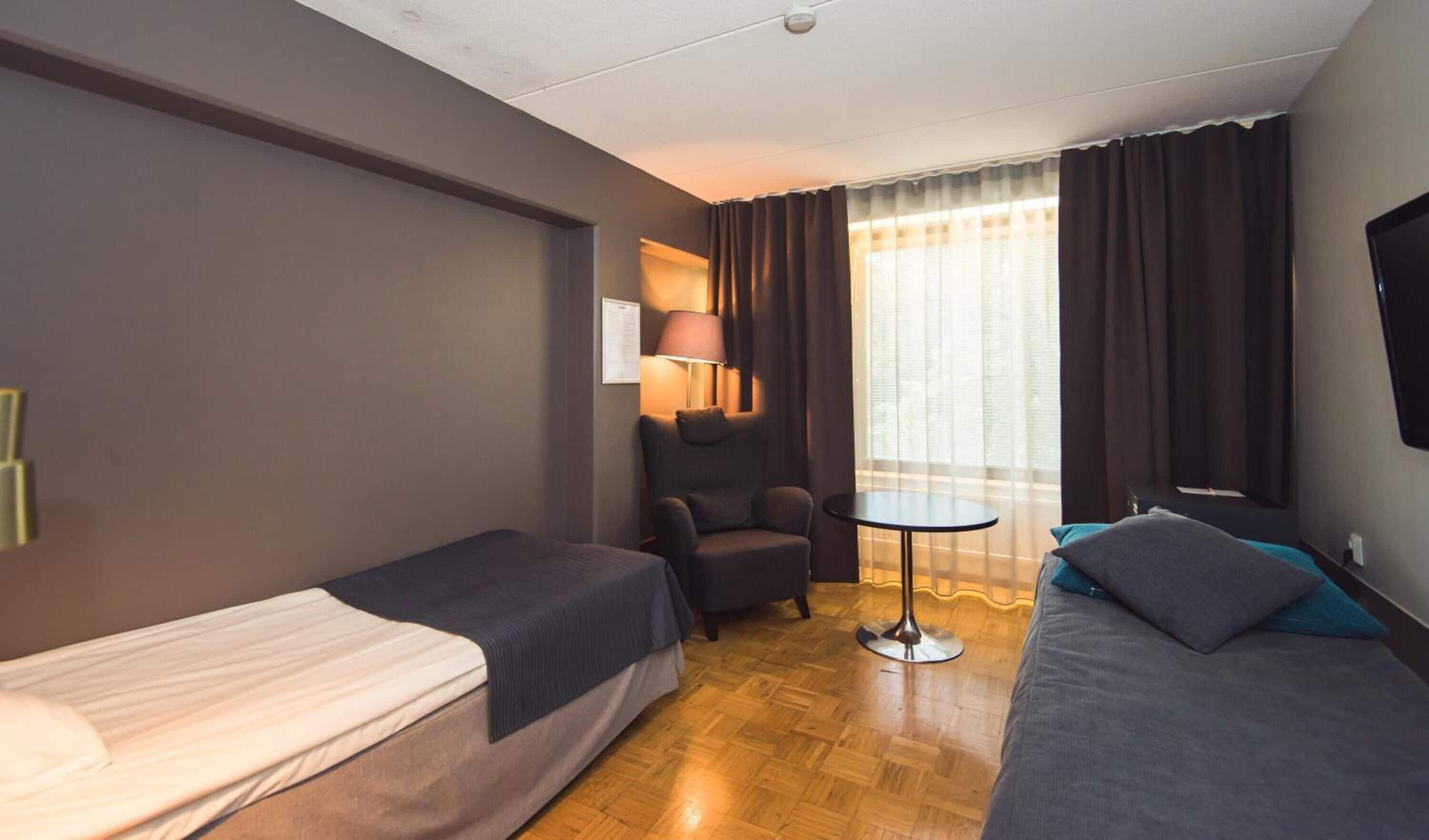 A hotel room with two single beds, a sofa, a small table, and a chair.