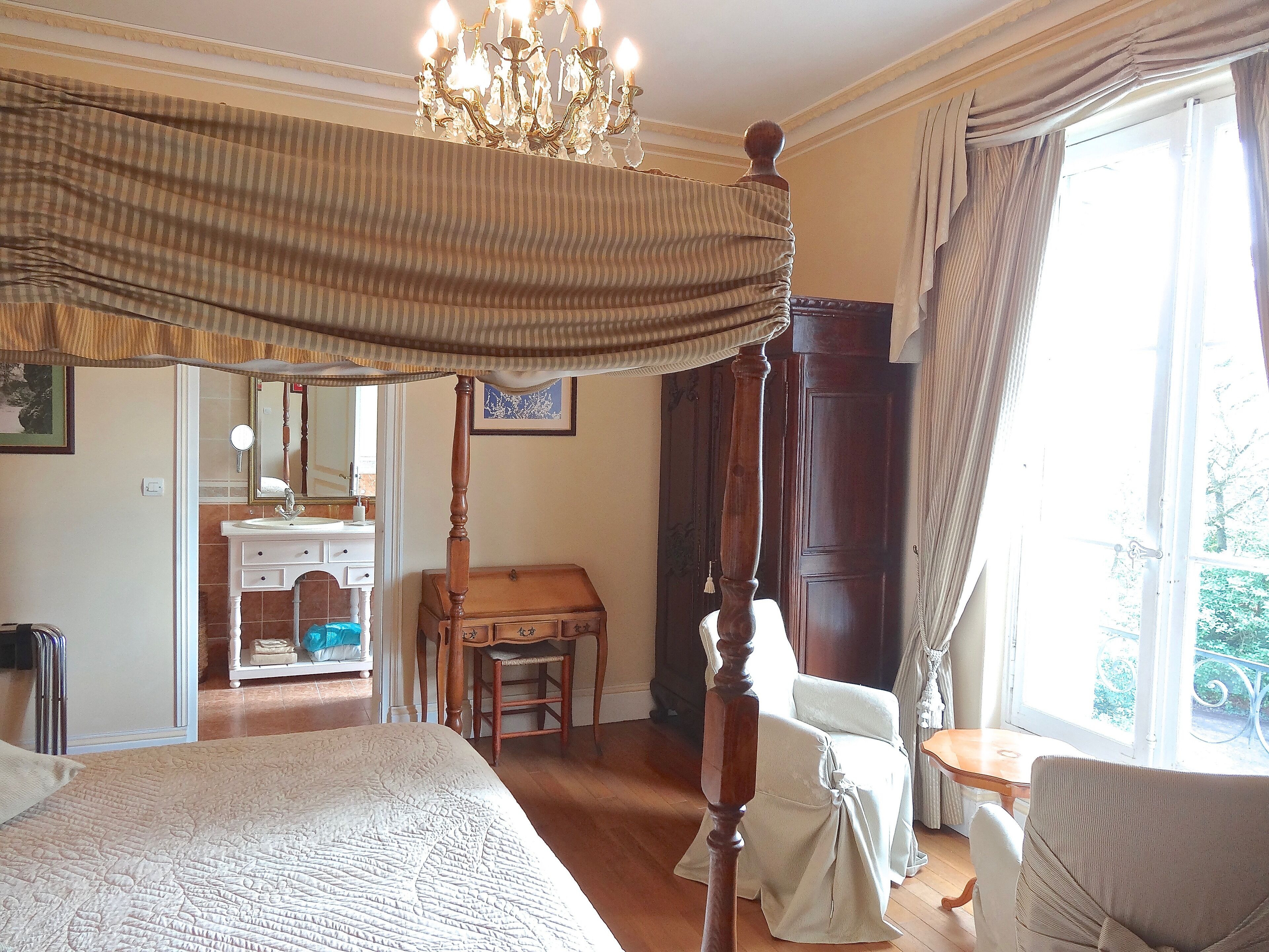 Een slaapkamer met een hemelbed, een houten stoel, een tafeltje en uitzicht op het landschap door een raam.