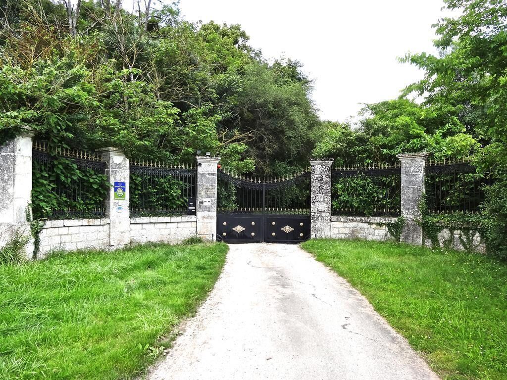 Una entrada con acceso restringido y un camino pavimentado que atraviesa un área verde exuberante.