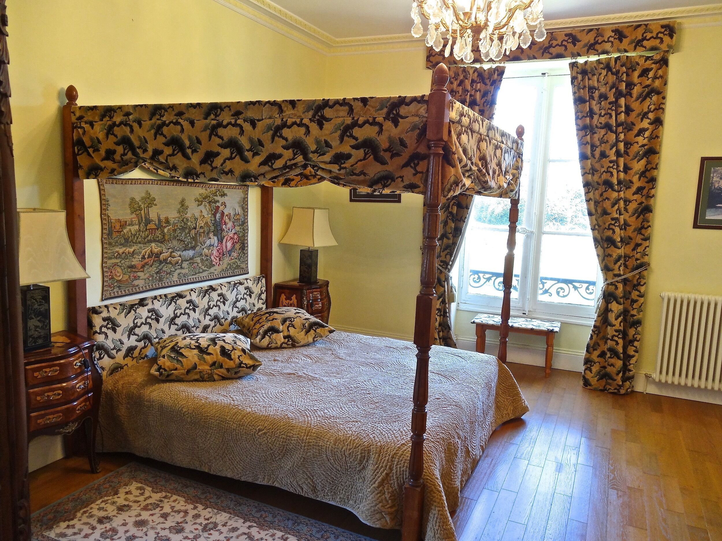 A four-poster bed with a canopy, a painting on the headboard, two bedside tables with lamps, and a window with curtains.