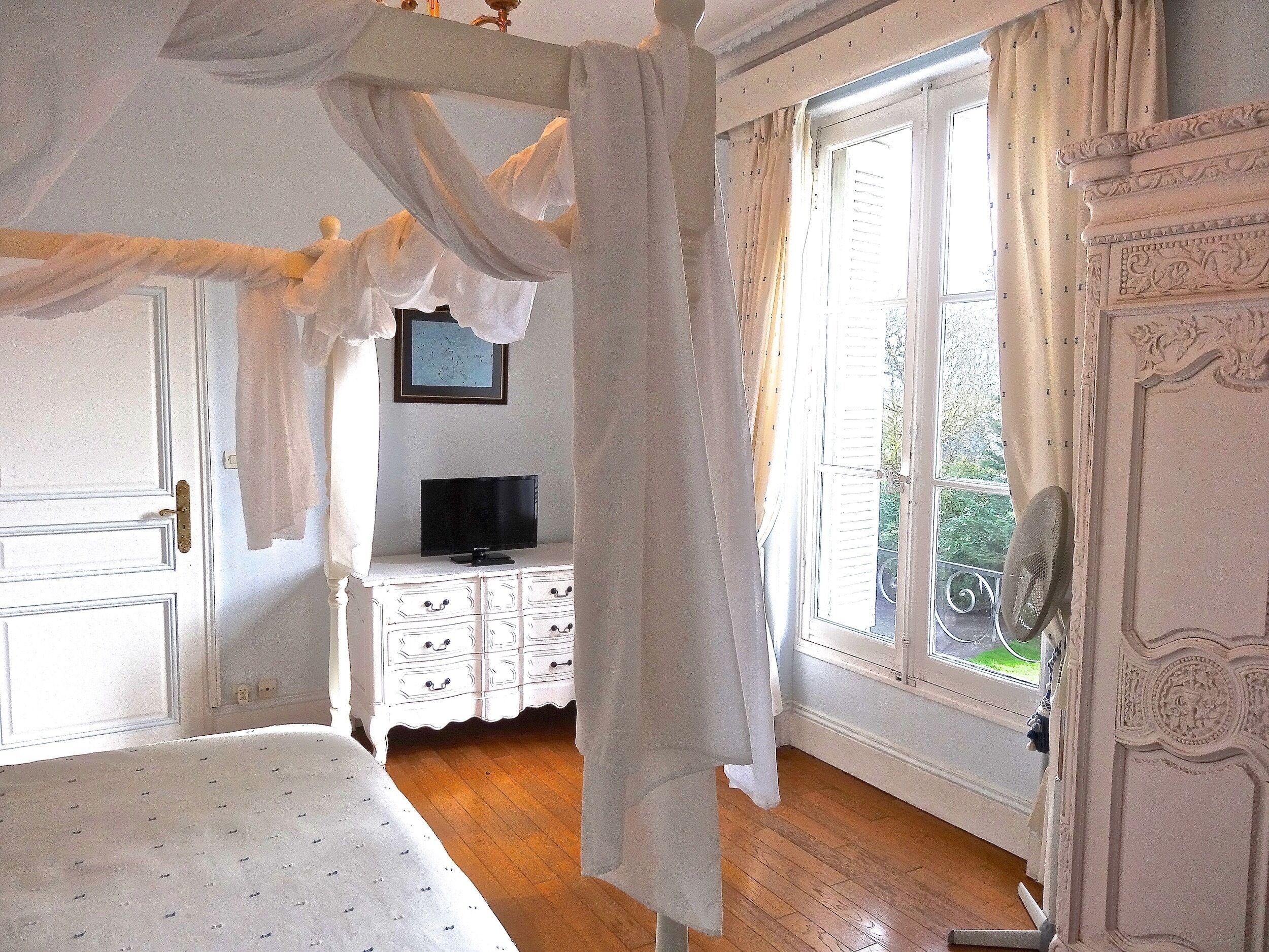 Una camera da letto con un letto a baldacchino, una televisione su un comò e un balcone con una sedia.