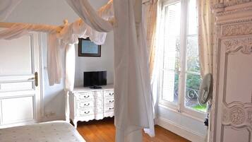 Una camera da letto con un letto a baldacchino, una televisione su un comò e un balcone con una sedia.