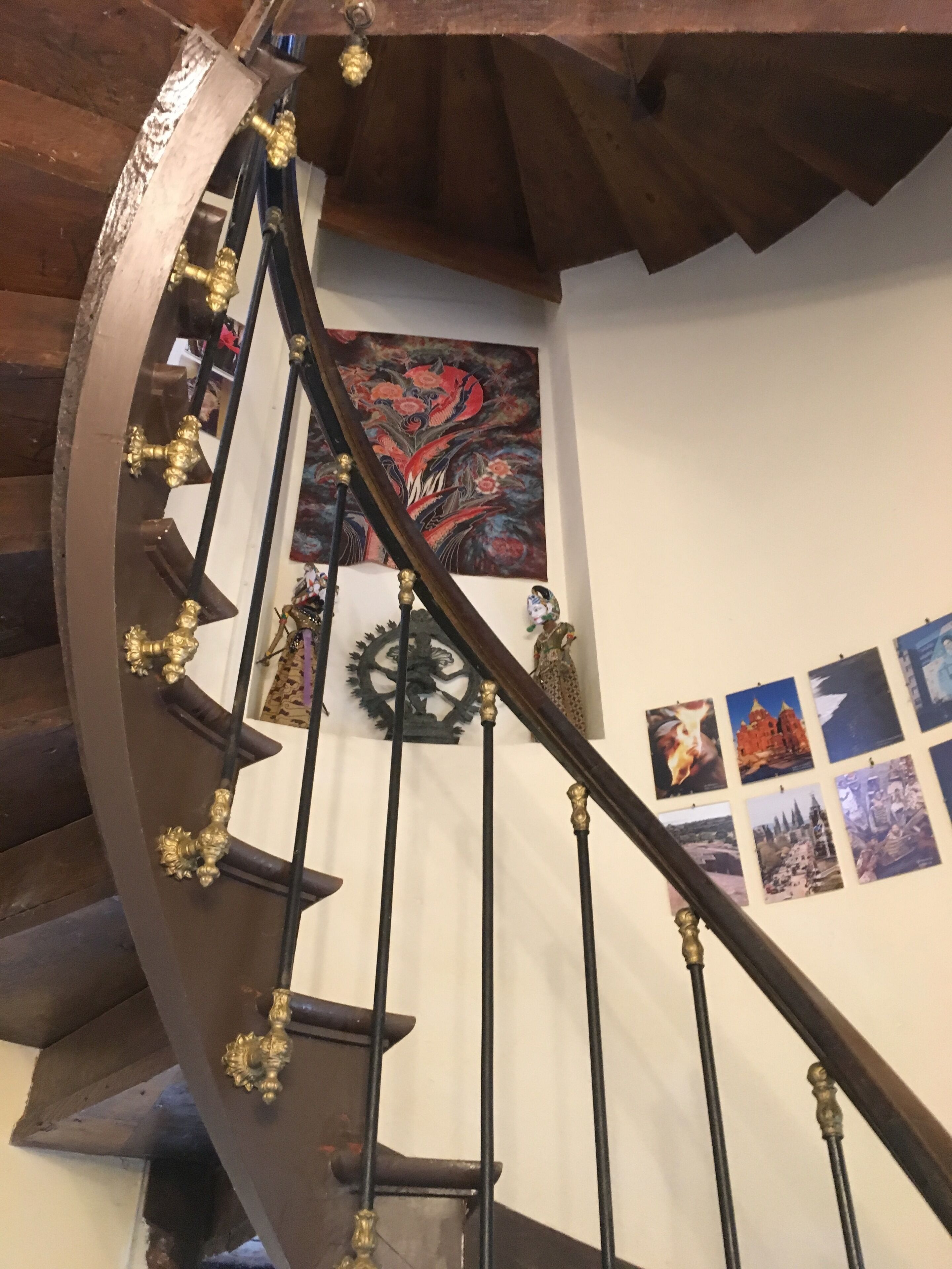 Un escalier en colimaçon orné de rampes en laiton et un mur décoratif agrémenté de tableaux encadrés.