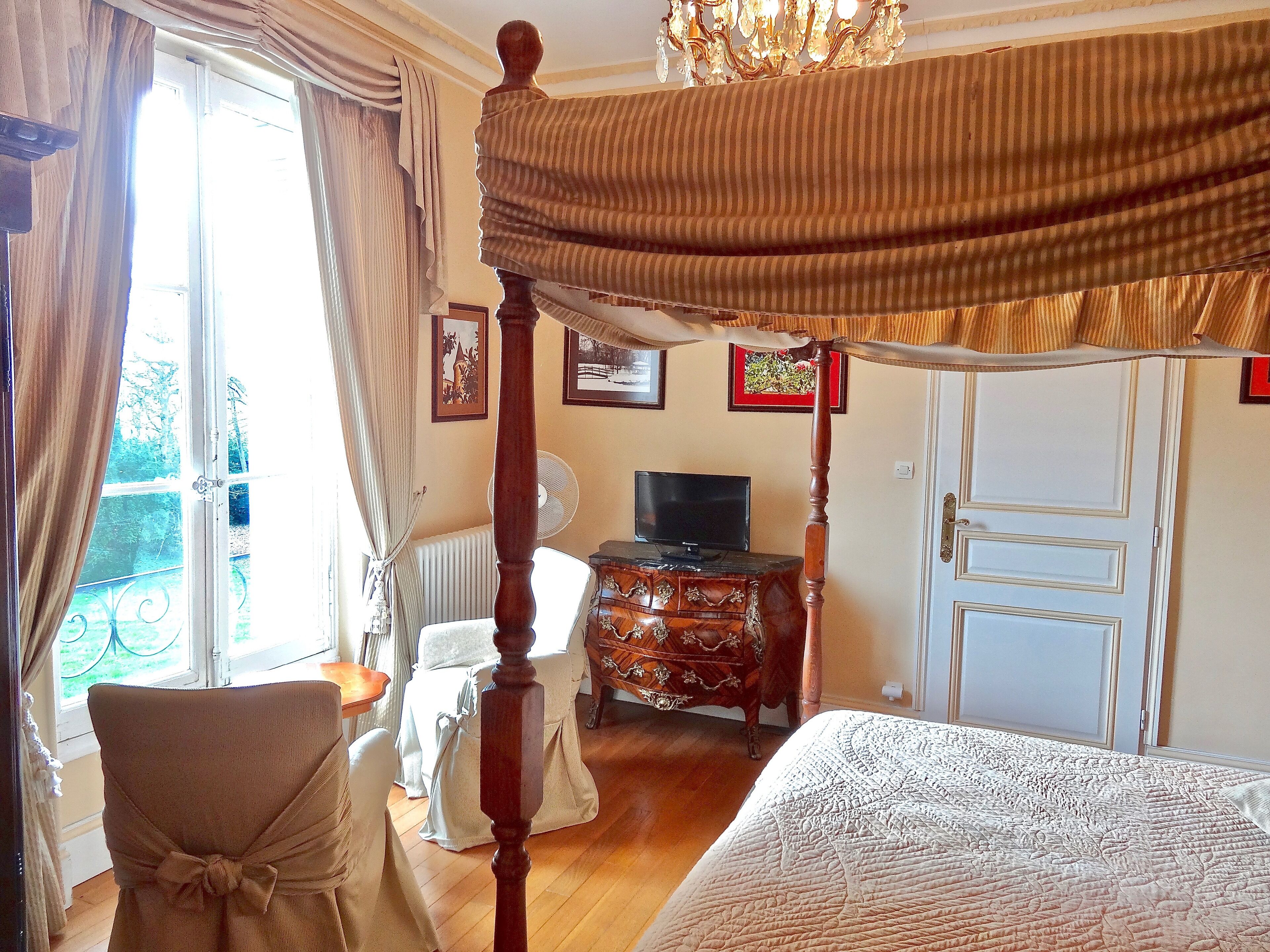 A bedroom with a four-poster bed, a television, a dresser, and a chair.