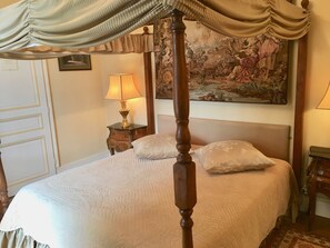 A four-poster bed with a canopy, a nightstand with a lamp, and a painting on the wall.