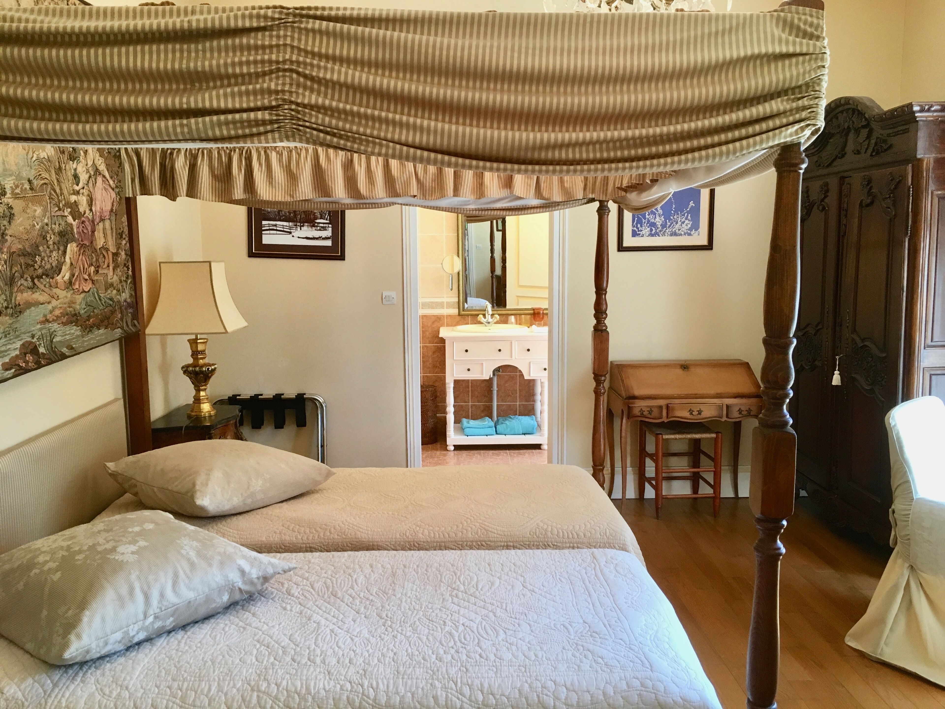A four-poster bed with a canopy, two pillows, a bedside lamp, a small table, and a chair.