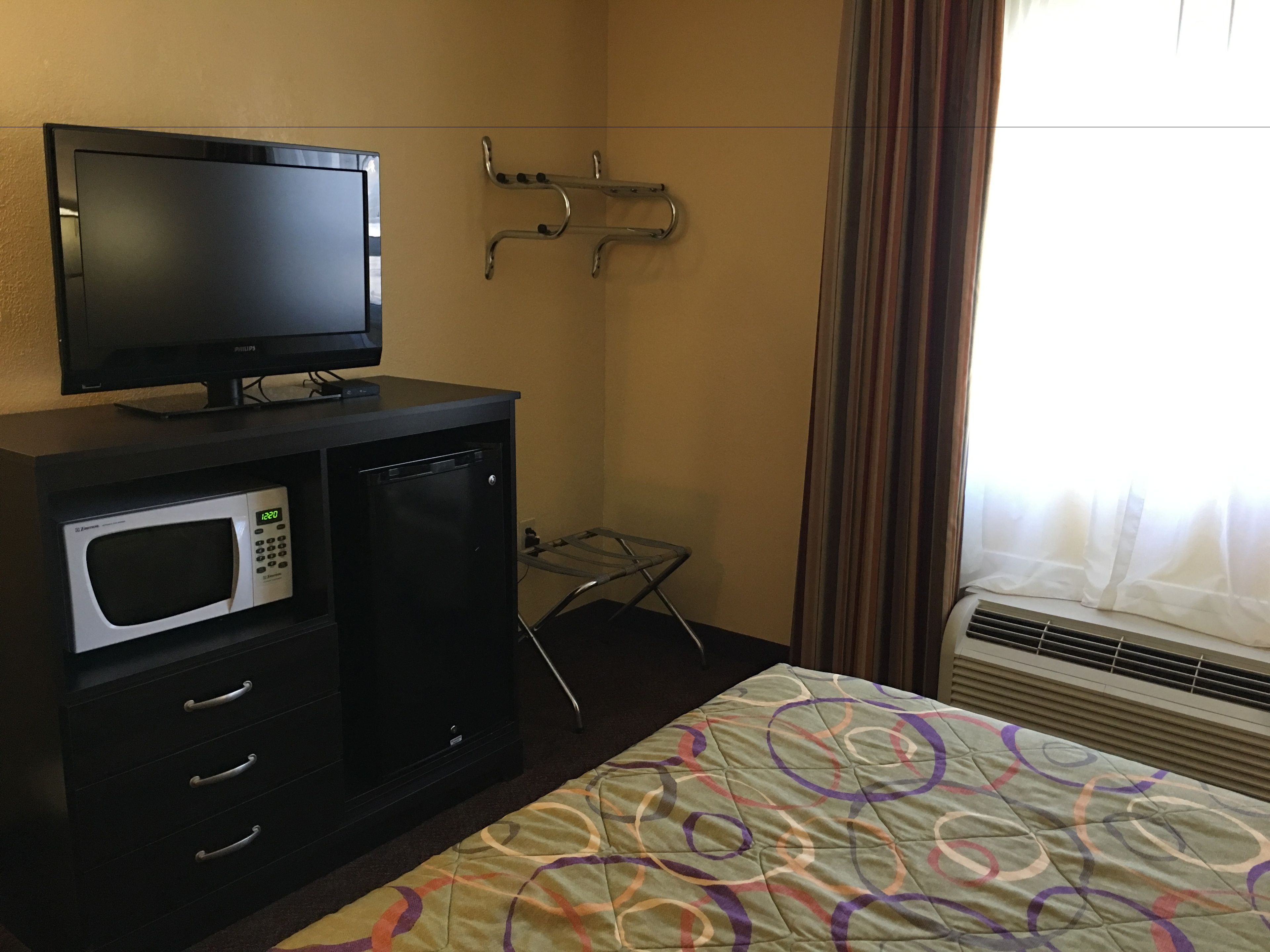 Une chambre d’hôtel avec un téléviseur posé sur un meuble noir, un four à micro-ondes, une petite table et un lit recouvert d’une courtepointe aux couleurs vives.
