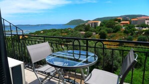 A balcony with a glass table and two chairs, overlooking a coastal landscape with buildings and greenery. - Résidence Hôtelière En Aparté (Porto-Vecchio)