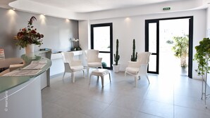 A reception area with a glass counter, white chairs, and potted plants. - Résidence Hôtelière En Aparté (Porto-Vecchio)