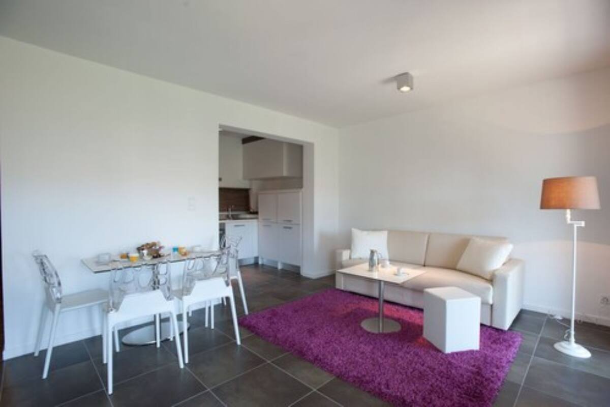 A modern living room with a white sofa, a dining table with chairs, and a purple rug.