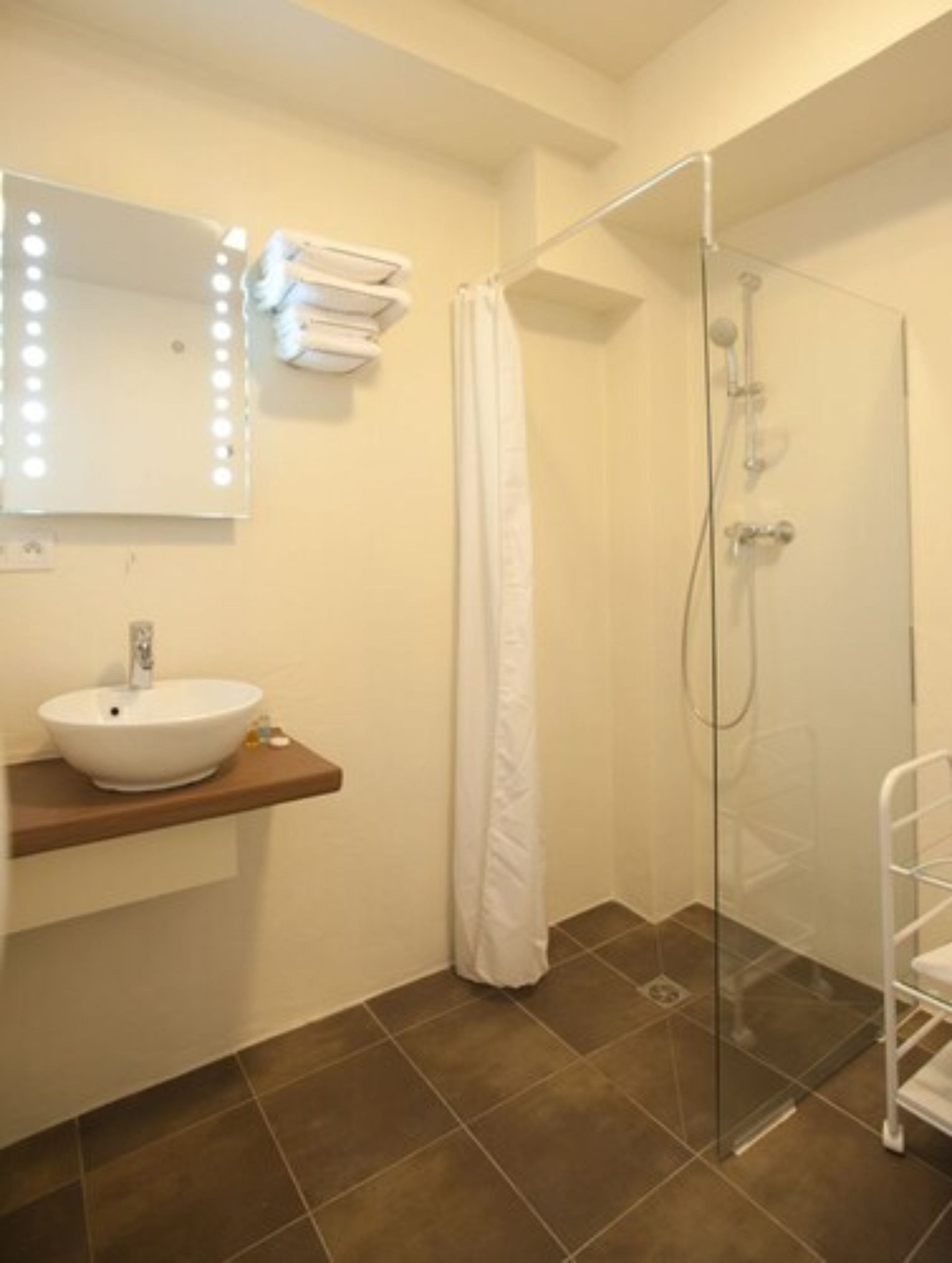 A bathroom with a white sink, a mirror with lights, a shower, and a towel rack.