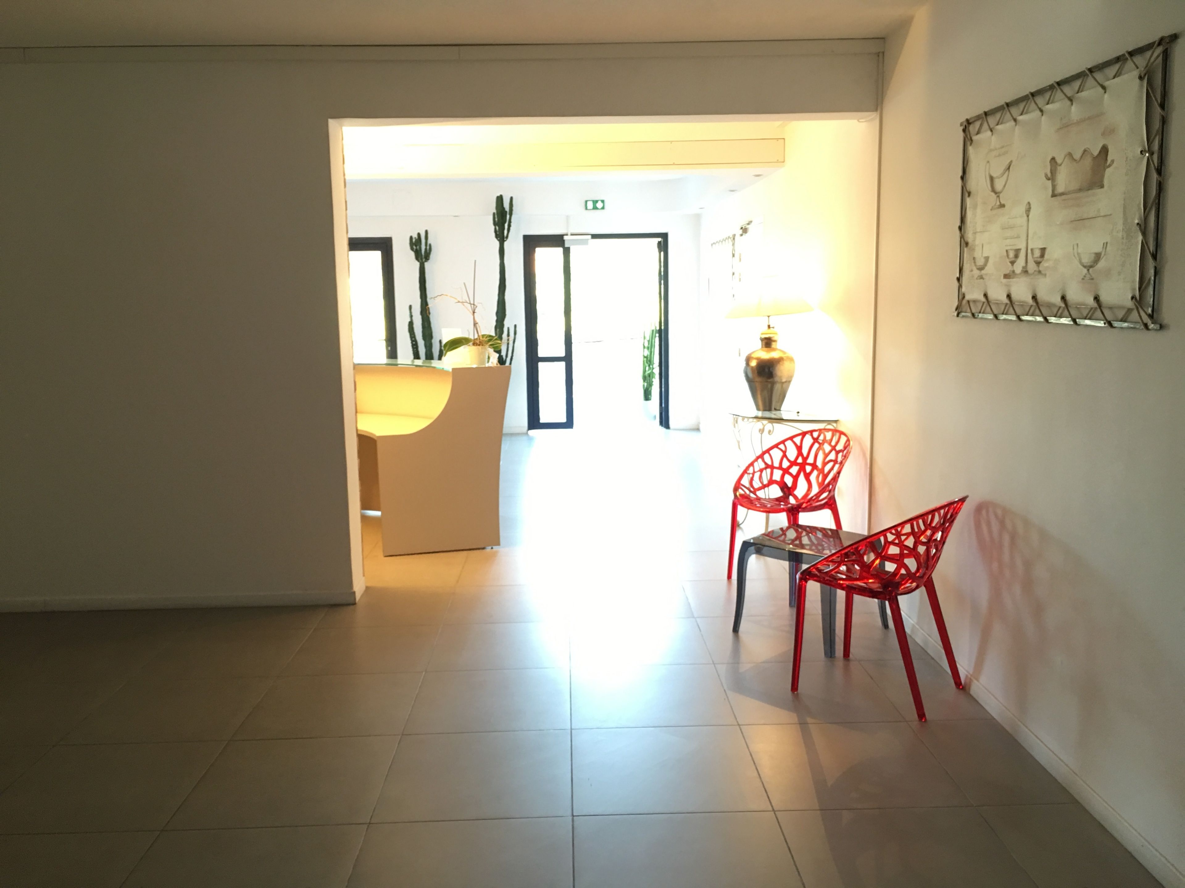A hotel lobby with a reception desk, a red chair, and a wall-mounted artwork.
