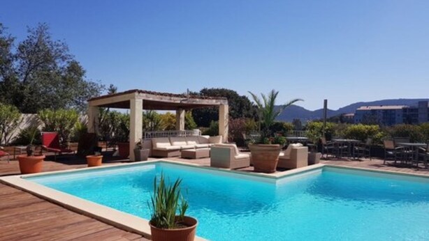A pool area with a wooden deck, lounge chairs, and a pergola. - Résidence Hôtelière En Aparté (Porto-Vecchio)