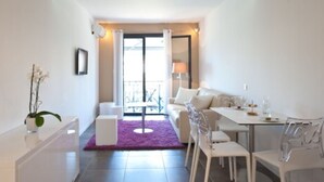 A modern, well-lit room with a dining area, a sofa, and a balcony with a view. - Résidence Hôtelière En Aparté (Porto-Vecchio)