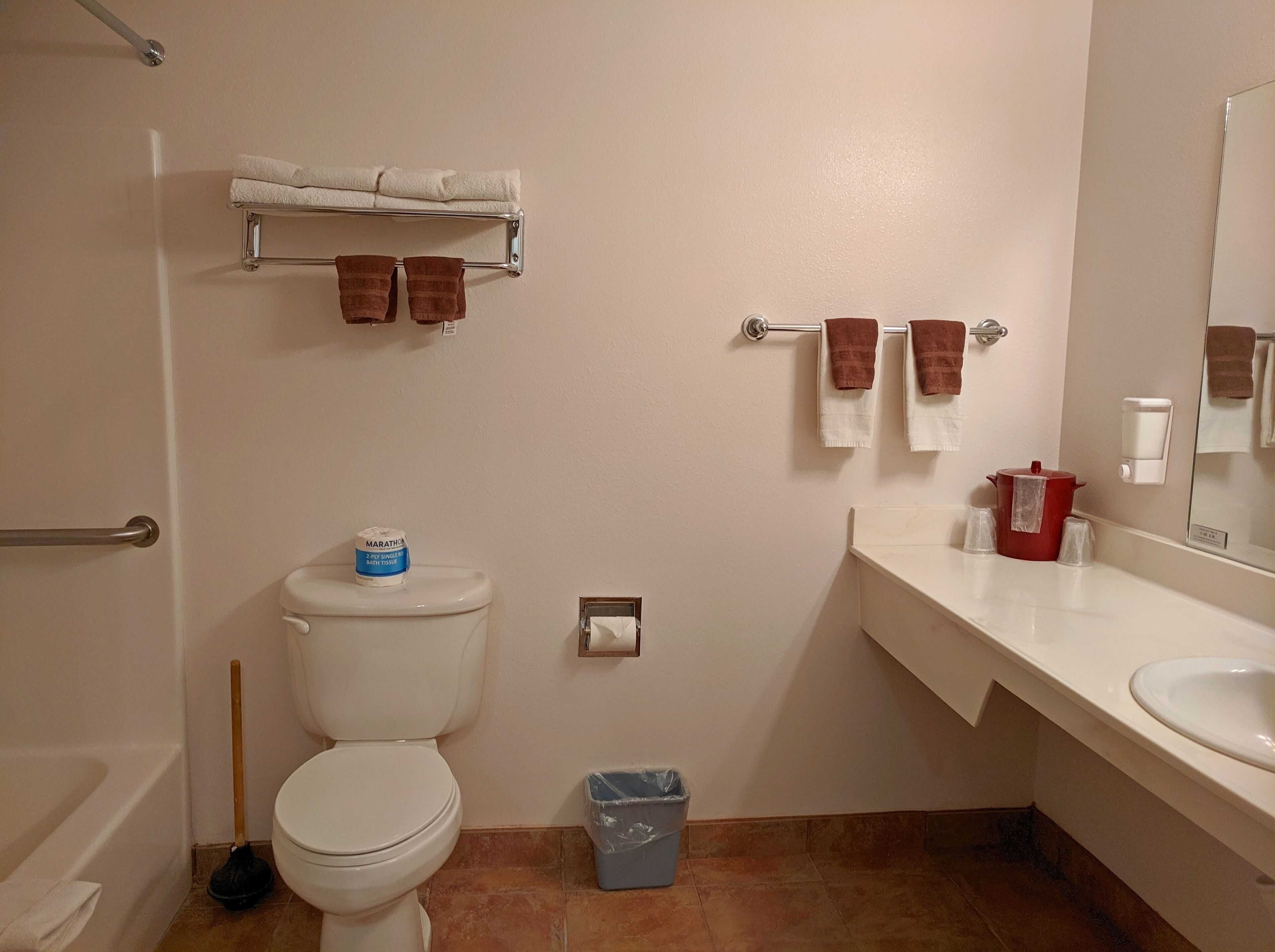 A bathroom with a toilet, a bidet, a hand dryer, a trash bin, and a towel rack with towels.