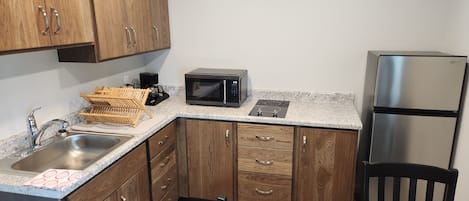 A kitchen with wooden cabinets, a stainless steel sink, a microwave, a refrigerator, and a dining table with chairs.