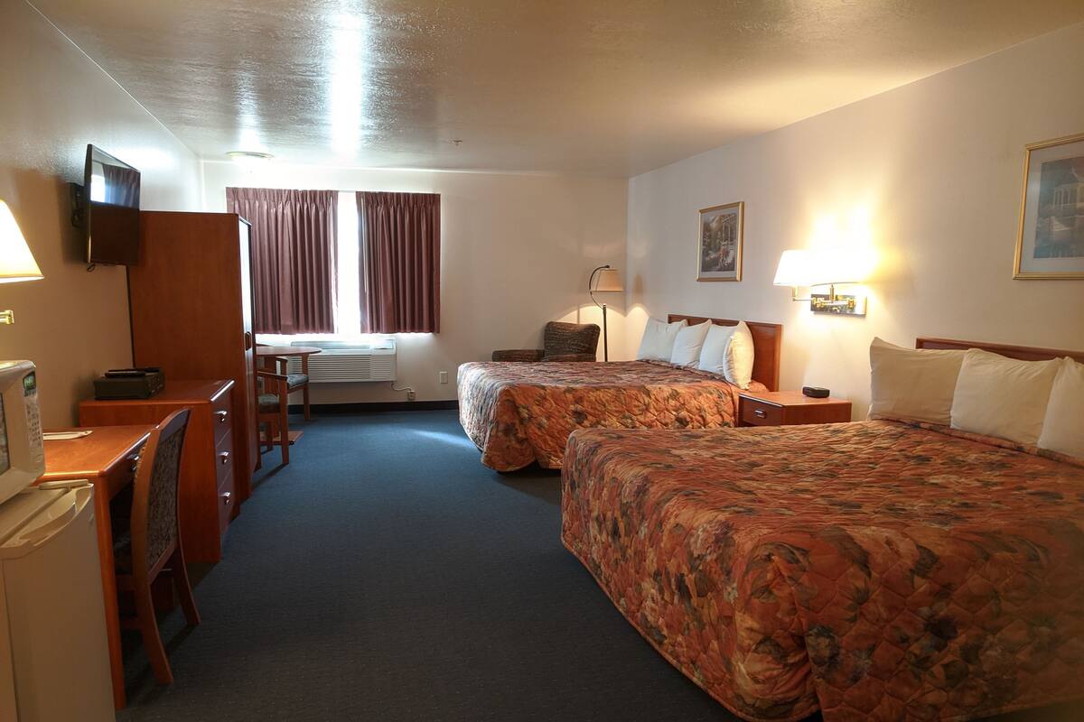 Ein Hotelzimmer mit zwei Betten, einem Schreibtisch, einem Stuhl, einem Fernseher und einem Fenster mit Vorhängen.