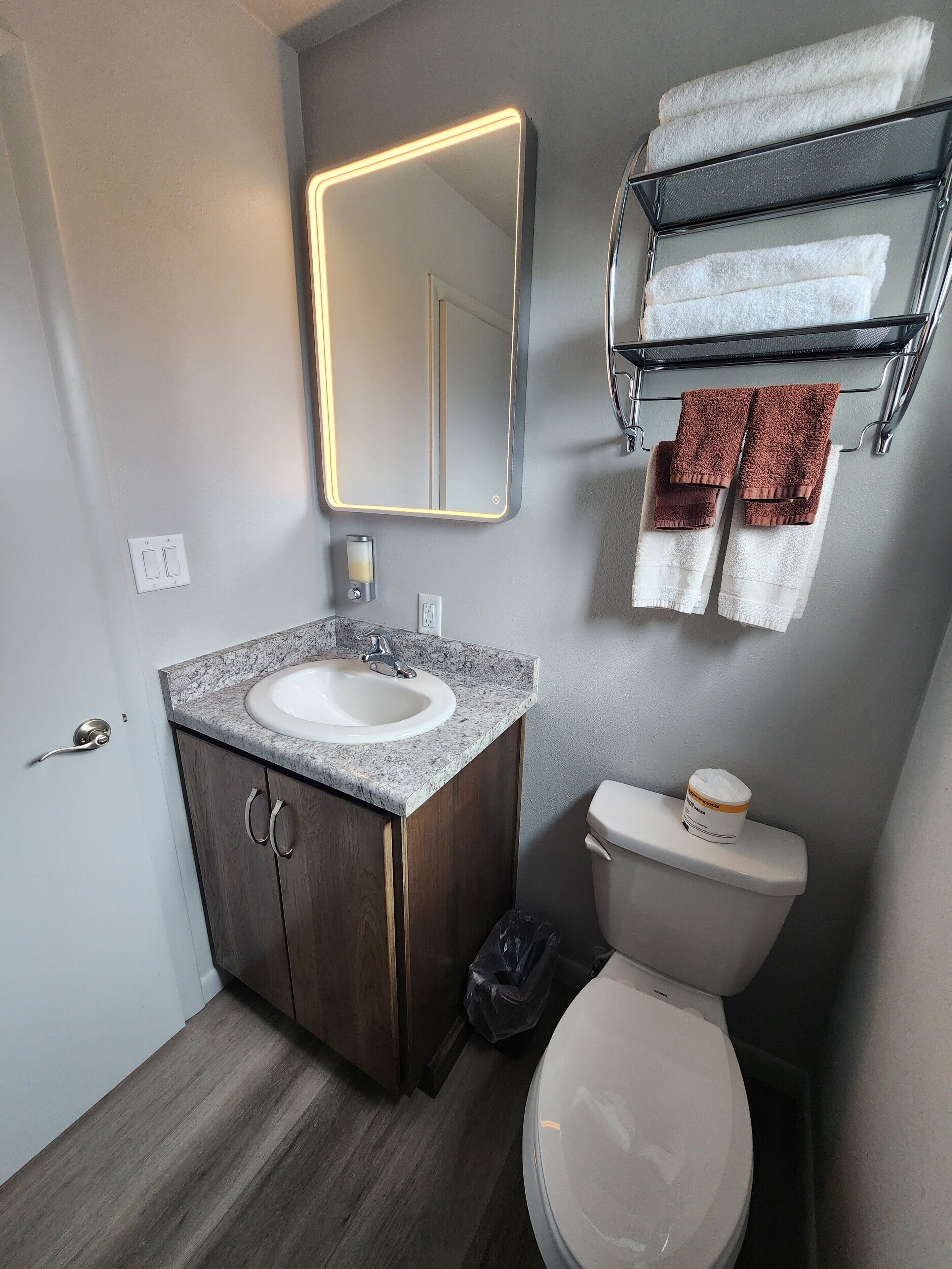 A modern bathroom with a marble sink, a mirror with backlighting, a toilet, and a towel rack with towels.