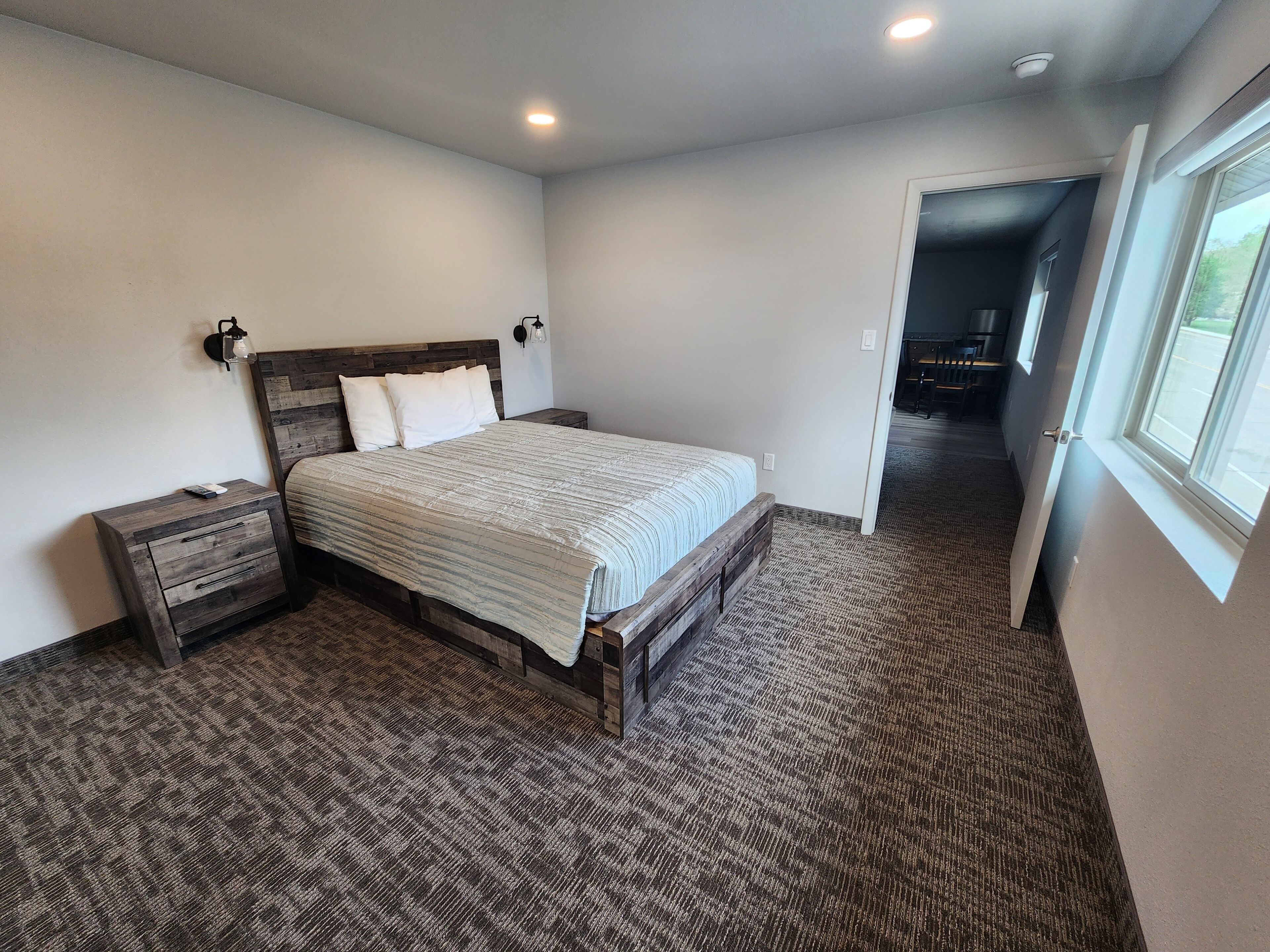 A bedroom with a wooden bed frame, a nightstand, and a carpeted floor.