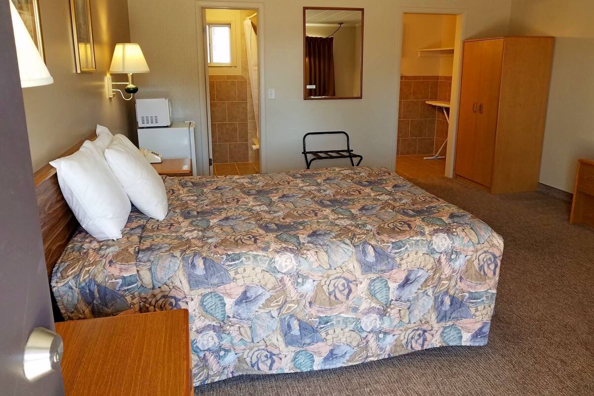 Ein Hotelzimmer mit einem großen Bett, einem Nachttisch, einer Lampe, einem Spiegel, einem Kleiderschrank und einer Badezimmertür.