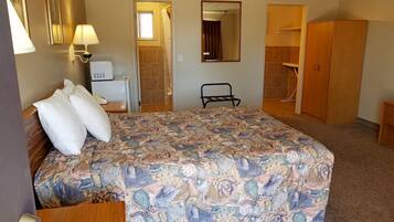 A hotel room with a large bed, a bedside table, a lamp, a mirror, a wardrobe, and a bathroom door.