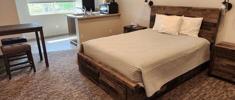 A bedroom with a wooden bed, a nightstand, a bedside table, a desk, and a chair.