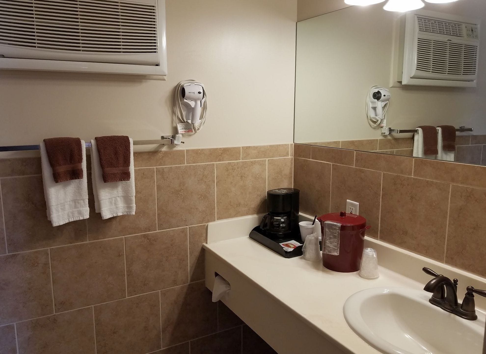 A bathroom with a sink, mirror, towel rack, and a coffee maker.